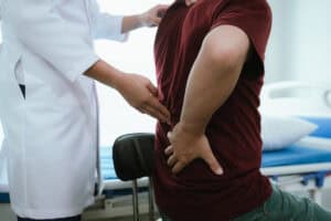 Doctor explaining spine anatomy with a model to a male patient experiencing lower back pain in a clinic discussing diagnosis and treatment options - Engelhardt Rechtsanwaltskanzlei - Engelhardt Rechtsanwaltskanzlei
